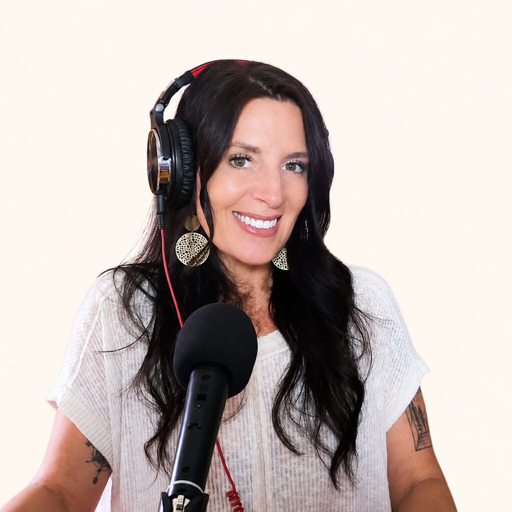 Annette Benedetti smiling while wearing headphones and speaking into a black podcast microphone against a pale cream background.